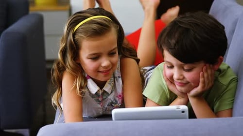 Two Children Lying on Couch Using Tablet Device