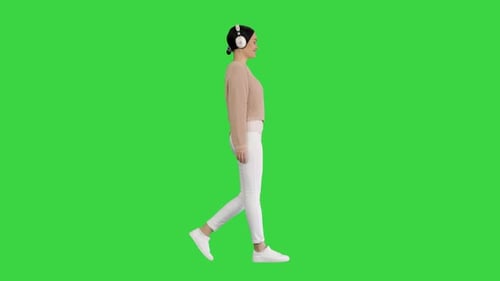 Young Woman with Headphones Walking Listening To the Music on a Green Screen, Chroma Key.