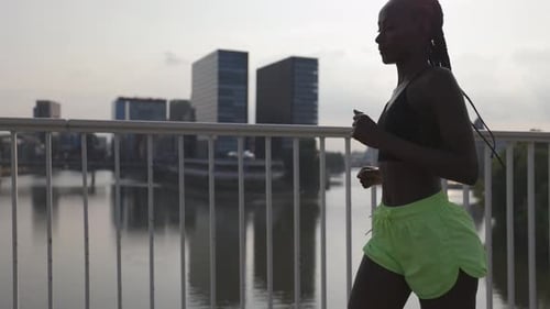 Active Woman in Sportswear Jogging on Bridge Over River