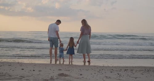 Young Family of Four Stand on the Sea Coast, Holding Hands Together