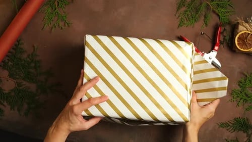 Woman wrapping holiday gift with evergreen decor