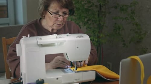Senior Woman Sewing Yellow Fabric Indoors