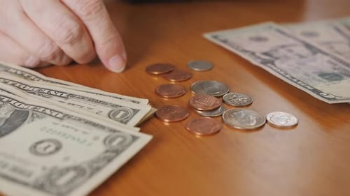Hand Counting US Coins Next to Dollar Bills