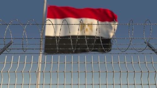 Blurred Waving Flag of Egypt Behind Barbed Wire Fence