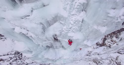 Aerial drone view of a man ice climbing on a frozen waterfall in the mountains.