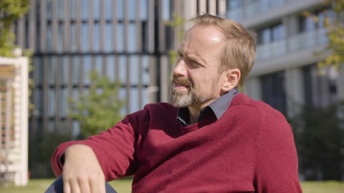 A Middleaged Handsome Caucasian Man Thinks About Something As He Sits in a Street in an Urban Area