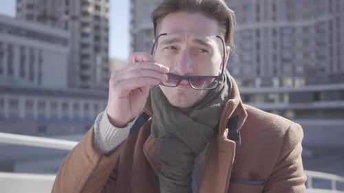 Portrait of a Handsome Stylish Man Wearing Sunglasses Sitting Against a Background of Urban