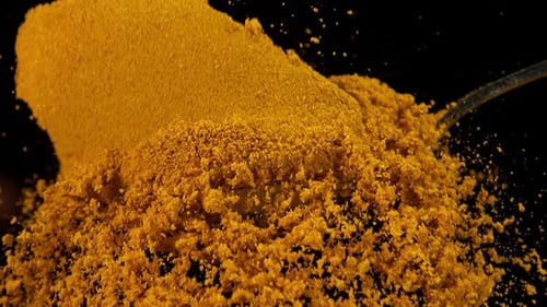 Spoon and Curry Powder falling against Black Background, Slow motion