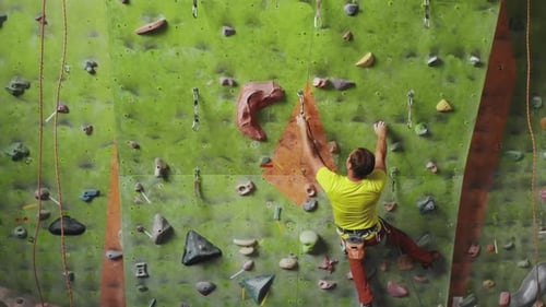 Male Climber Climbs the Cliff Wall in the Room Reaching and Gripping Hold