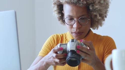 Afro Female Photographer Looks at Photos on Camera While Working in an Office