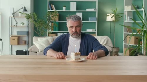 Man Sits With Birthday Cake and Candle