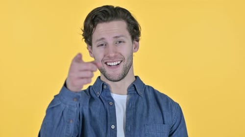Young Man Points and Smiles on Yellow Background