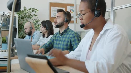 Callcenter-Mitarbeiter chatten mit Kunden und arbeiten mit Computern, die an Schreibtischen in Innenräumen tippen