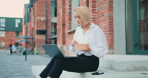 Frau isst Gemüsesalat zum Mittagessen, sitzt auf der Treppe während der Benutzung des Laptops