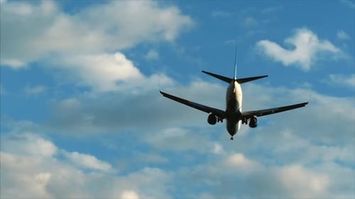 Plane Flies in a Blue Sky with Clouds Overhead, Preparing To Land at the Airport at Sunset