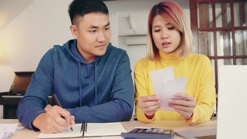 Young couple managing finances, reviewing their bank accounts using laptop and calculator at home