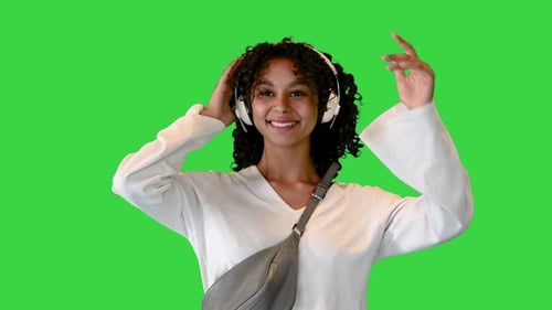 Smiling Young African American Woman Walking and Listening To Music on Headphones on a Green Screen