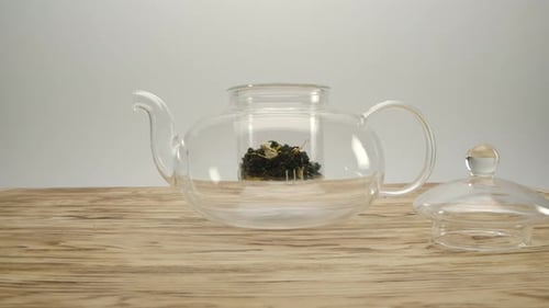 Glass Teapot with Tea Leaves on Wood Table