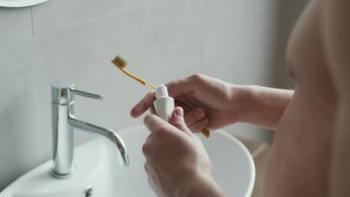 Squeezing Toothpaste on Bamboo Toothbrush in Bathroom