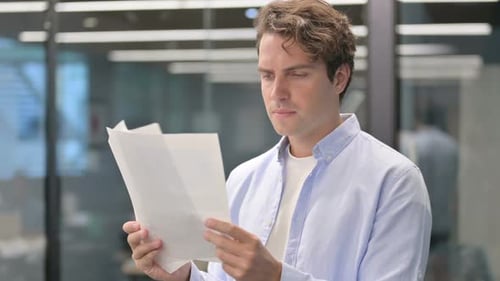 Young Adult Reviews Documents in Modern Office