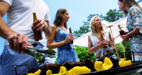 Group of friends having a bottle of beer while preparing barbeque