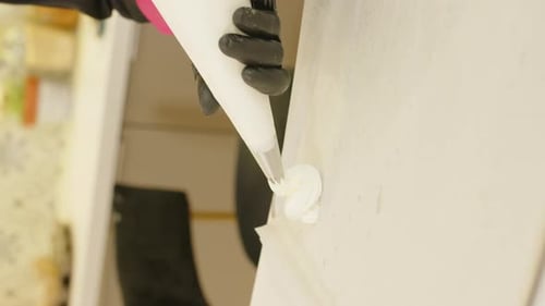 Vertikale Nahaufnahme von Händen mit Spritzbeutel formender Pavlova. Flacher Fokus