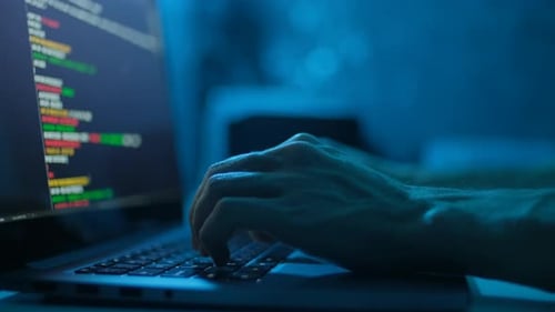 Hacker arbeitet nachts am Laptop, Hände geben einen Viruscode auf der Tastatur oder Hacking-Website ein