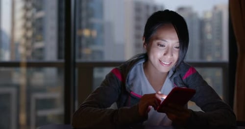 Woman Smiling Using Phone at Home at Night