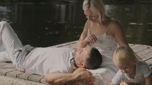 Young Family Mom Father and Son Are Sitting on the Pier Near the River on a Sunny Day