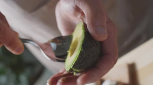 Hands Removing Avocado from Skin with Spoon