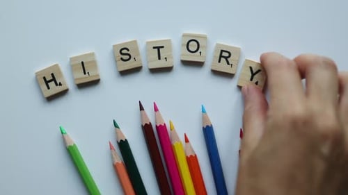 Hand Composing Word History with Wooden Letters and Colorful Pencils on White Background