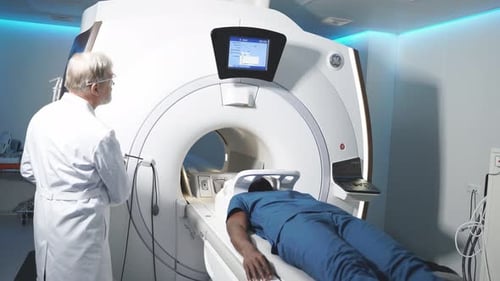 In Medical Laboratory Senior Radiologist Controls MRI or CT or PET Scan with Male Patient Undergoing