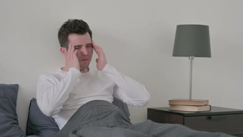 Man Having Headache While Sitting in Bed