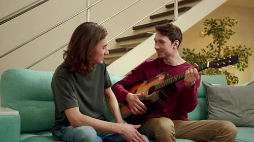 Two Young Adults Playing Acoustic Guitar on Sofa