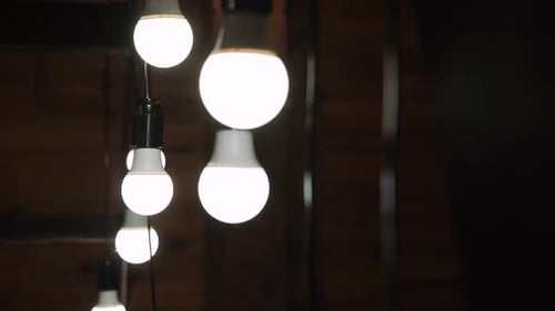 Garland of Large Light Bulbs on Black Wire Swings in Wooden House Closeup