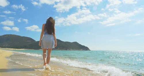 Attractive Female Walking Along Sandy Beach. Clear Blue Water