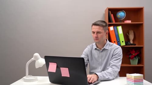 Young Guy Office Worker Manager is Typing in the Computer and on a Paper Sticker