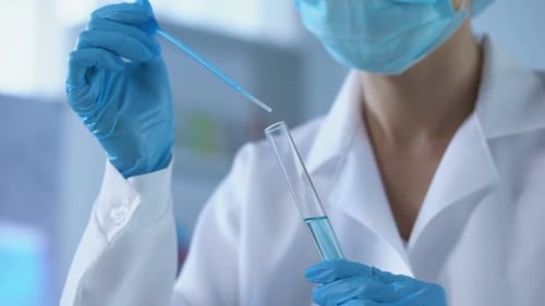 Une travailleuse de laboratoire dégoulinant un liquide bleu dans un tube à essai et analysant