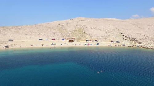 Flying above umbrellas and people on isolated beach of Pag island, Croatia
