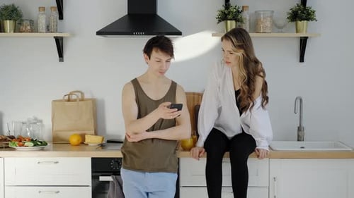 Couple Talking in Kitchen, Man Using Phone