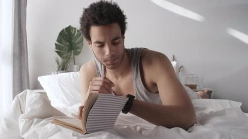 Man Reading a Book in Bed During Daytime