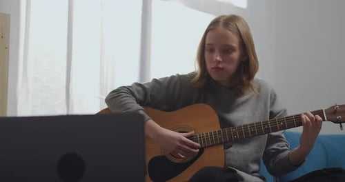 Girl Learning Guitar at Home Using Laptop