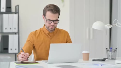 Young Adult Using Tablet with Laptop at Desk