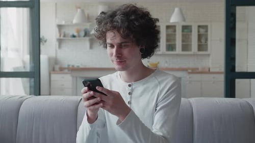 Young Adult Smiling While Using Smartphone at Home