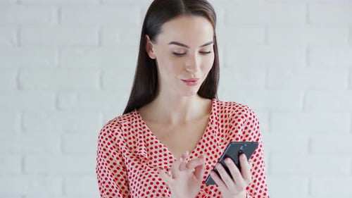 Woman Using Mobile Phone in Front of White Wall