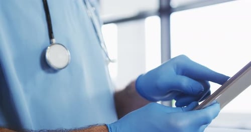 Caucasian male doctor wearing protective gloves using digital tablet