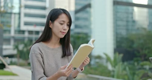 Young Woman Reading a Book Outdoors in the City