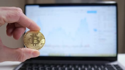Golden Bitcoin Held in Front of Trading Laptop
