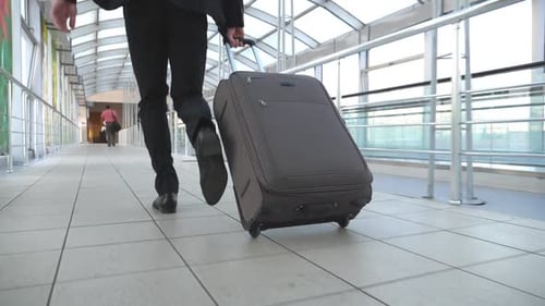 Legs of Successful Businessman Running in Hall of Terminal and Pulling Suitcase on Wheels. Camera