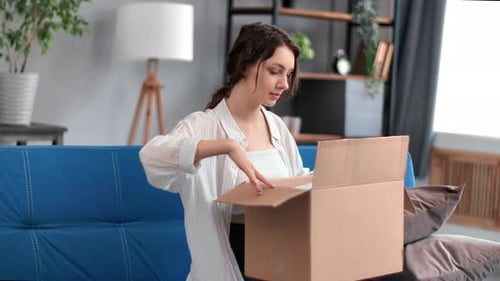 Excited Woman Opening Delivery Box on Couch Indoors